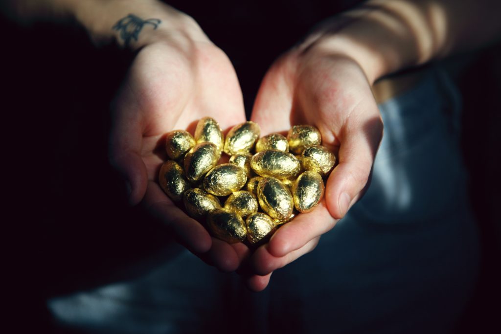 person holding gold wrapped chocolate eggs. The metaphor of money.