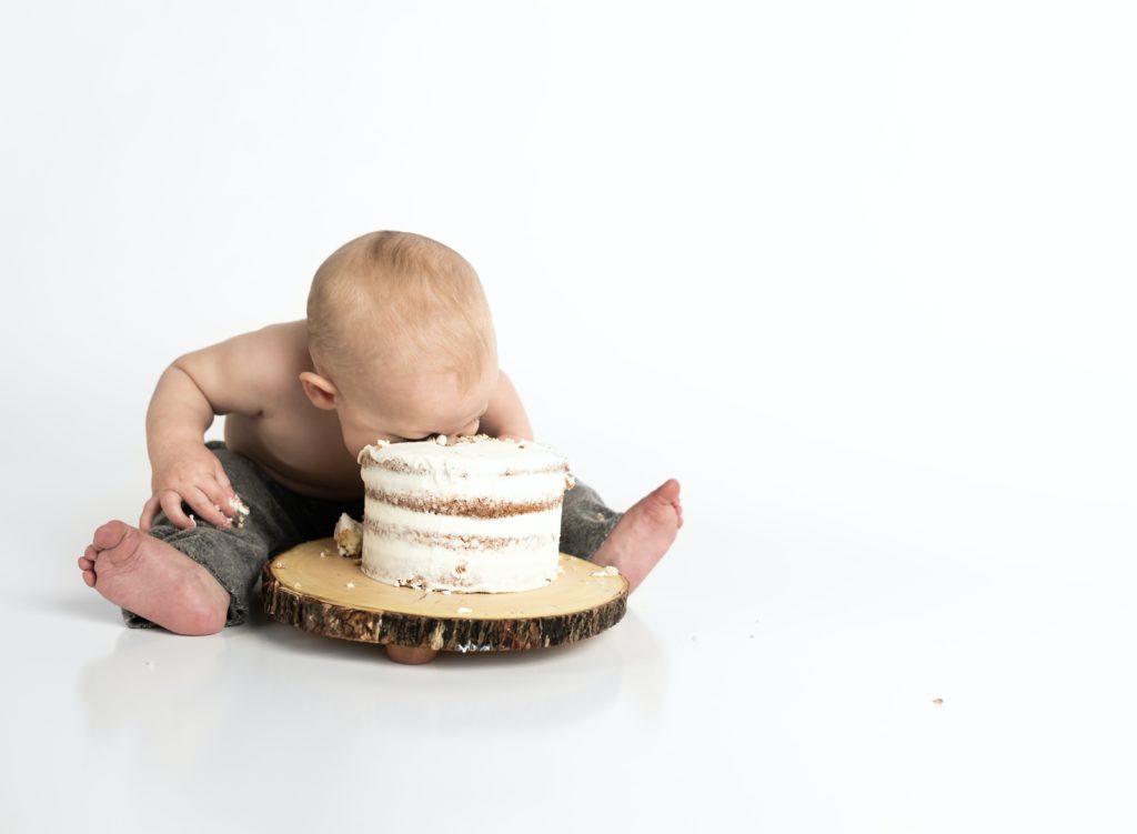 kid sitting beside round cake eating face first out of that cake. You could say that baby is greedy.