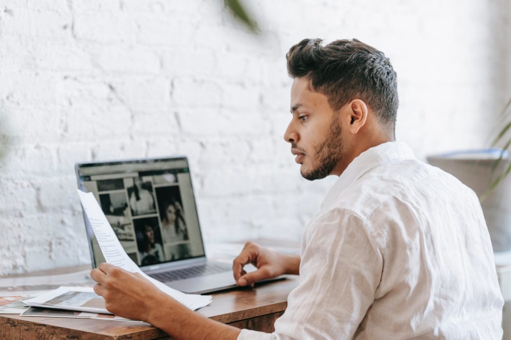 ethnic man reading document and working on laptop 