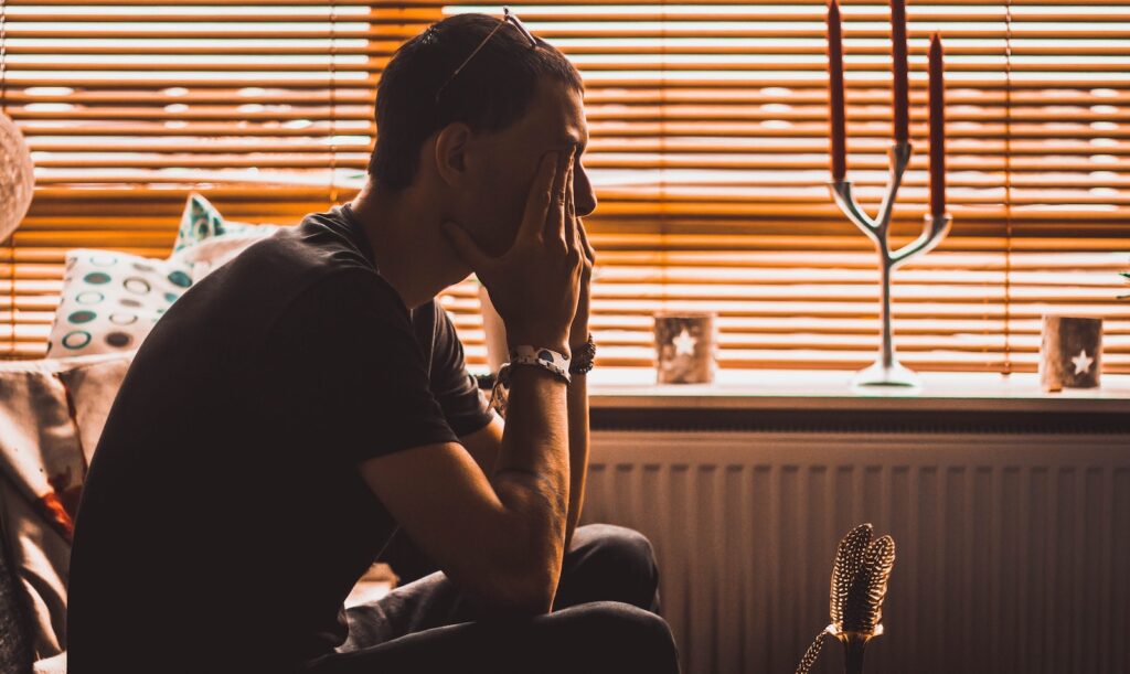 man sitting on chair covering his eyes contemplating his struggle