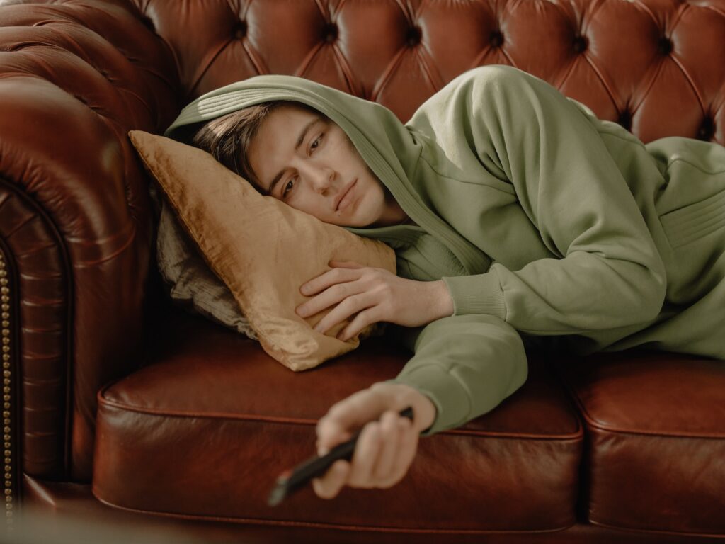 Woman in Gray Hoodie Lying on Brown Leather Couch
